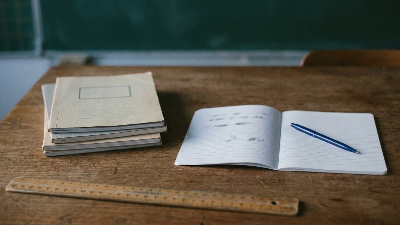 Cahiers empilés et cahier ouvert sur un bureau d'enseignant, dans une salle de classe vide